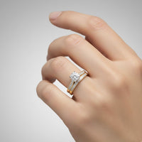 A hand with neatly manicured nails wears the 3/8 CTW 10k Yellow Gold Wedding Trio Set, featuring a dazzling diamond engagement ring and a matching gold wedding band adorned with small diamonds. This elegant trio is beautifully showcased against a plain gray background.