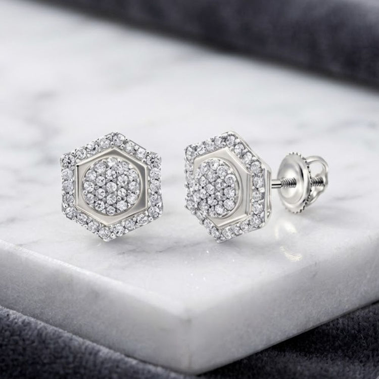 Sterling Silver Diamond Hexagon Cluster Earrings 1/3 Cttw are displayed on a white marble surface, featuring pavé-set diamonds in a hexagonal design with secure screw-back posts. These elegant earrings glisten under soft lighting, showcasing their sparkling diamond clusters.