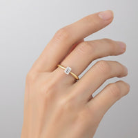 A hand adorned with the 1/4CT Diamond Emerald Solitaire Ring in 14K gold, set against a light gray background.