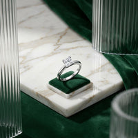 The 14k White Gold Princess Diamond Bridal Ring 3/4 Cttw is elegantly showcased on a petite green velvet box atop a marble surface, with green velvet and ribbed glass details in the background—the perfect bridal piece for making an elegant statement.