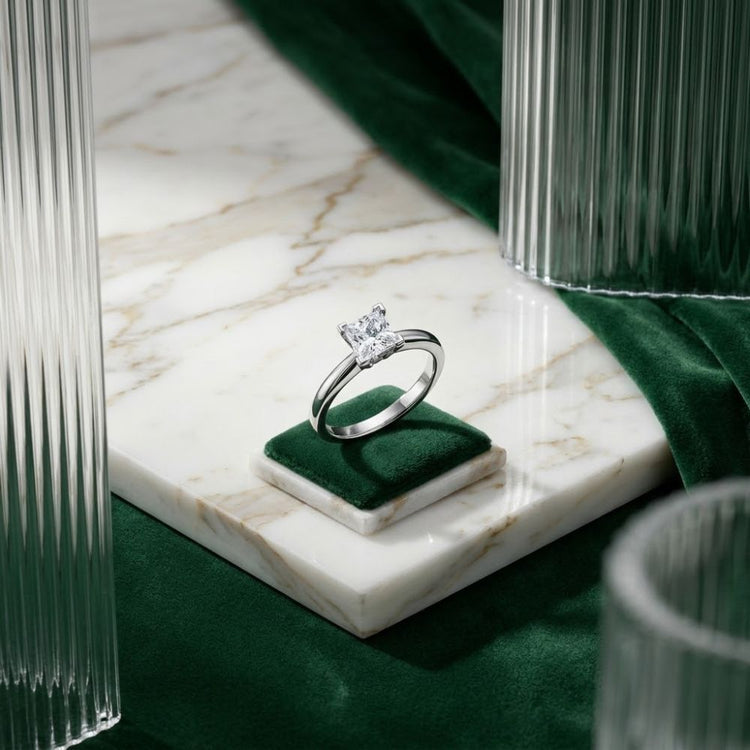 The 14k White Gold Princess Diamond Bridal Ring 3/4 Cttw is elegantly showcased on a petite green velvet box atop a marble surface, with green velvet and ribbed glass details in the background—the perfect bridal piece for making an elegant statement.