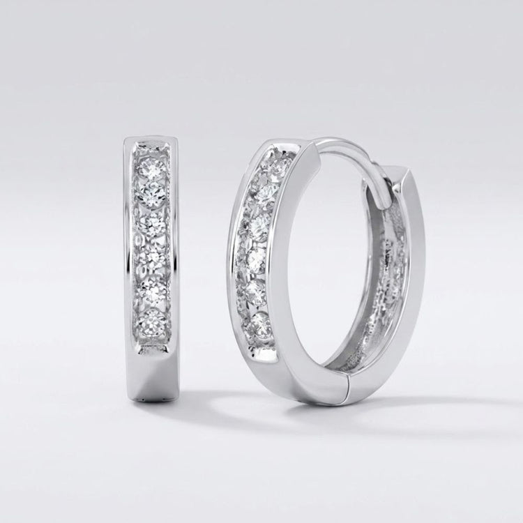 The 1/8CTW Round Diamond Hoop Channel Earrings in 10K yellow gold are displayed on a plain light gray background, with one earring upright and the other lying on its side to show both front and side views.