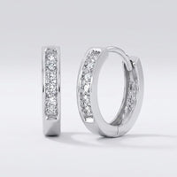 The 1/8CTW Round Diamond Hoop Channel Earrings in 10K yellow gold are displayed on a plain light gray background, with one earring upright and the other lying on its side to show both front and side views.