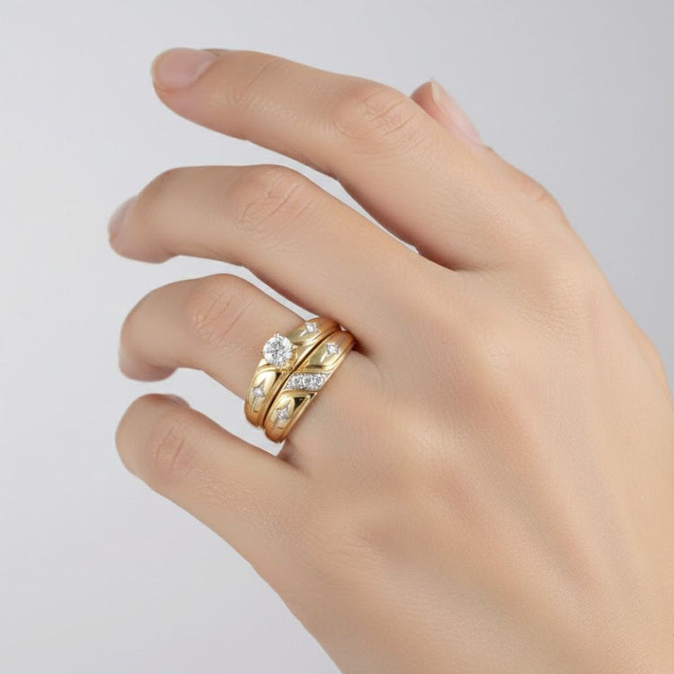A hand with neatly manicured nails wears three gold rings, including a 10k Gold Diamond Matching Wedding Ring Set alongside a sleek plain band, against a light background.