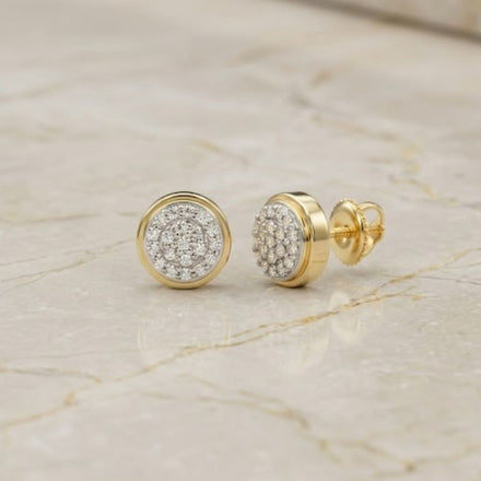 A pair of 1/10CTW Natural Diamond Round Gift Earrings in 10K gold rests elegantly on a polished marble surface.