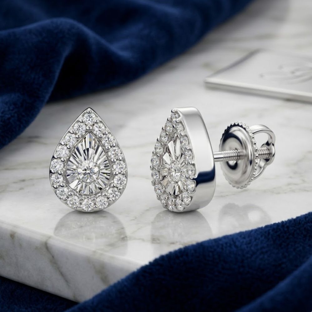 The 1/10CTW Natural Diamond Pear Earrings in 10K Gold feature a central stone surrounded by smaller diamonds, beautifully displayed on marble beside blue velvet fabric.