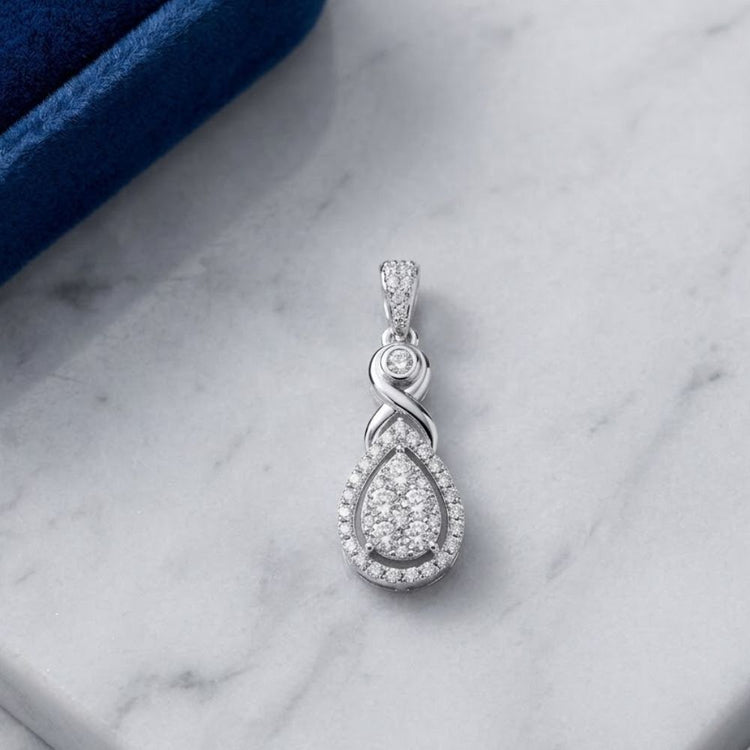 The 10K White Gold 1/2 CTW Diamond Cluster Pendant features a teardrop design with a halo of round diamonds, diamond bail, and detailed top, displayed on white marble next to a blue box.