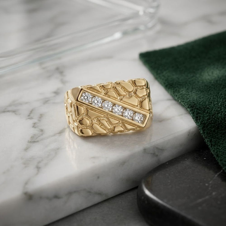 A 10k Yellow Gold Round Diamond Nugget Fashion Ring (1/2 Cttw), featuring a textured, cracked design and a diagonal row of seven sparkling diamonds, rests on a marble surface beside a green cloth.