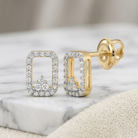 The 1/6CTW Natural Diamond Earrings 10K Gold, rectangular studs adorned with natural diamonds, are displayed on a marble surface—one standing upright and the other lying flat.