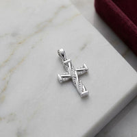 The 1/20 CTW Diamond Cross Pendant in 10K Gold sparkles with small natural diamonds as it rests on a white marble surface beside the edge of a burgundy velvet box.