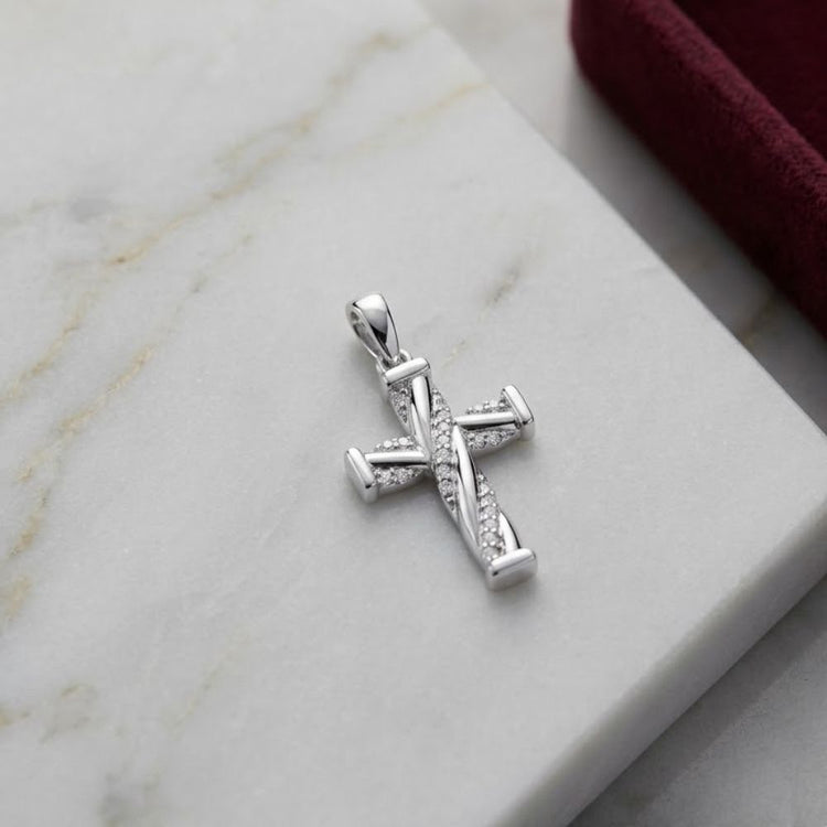 The 1/20 CTW Diamond Cross Pendant in 10K Gold sparkles with small natural diamonds as it rests on a white marble surface beside the edge of a burgundy velvet box.