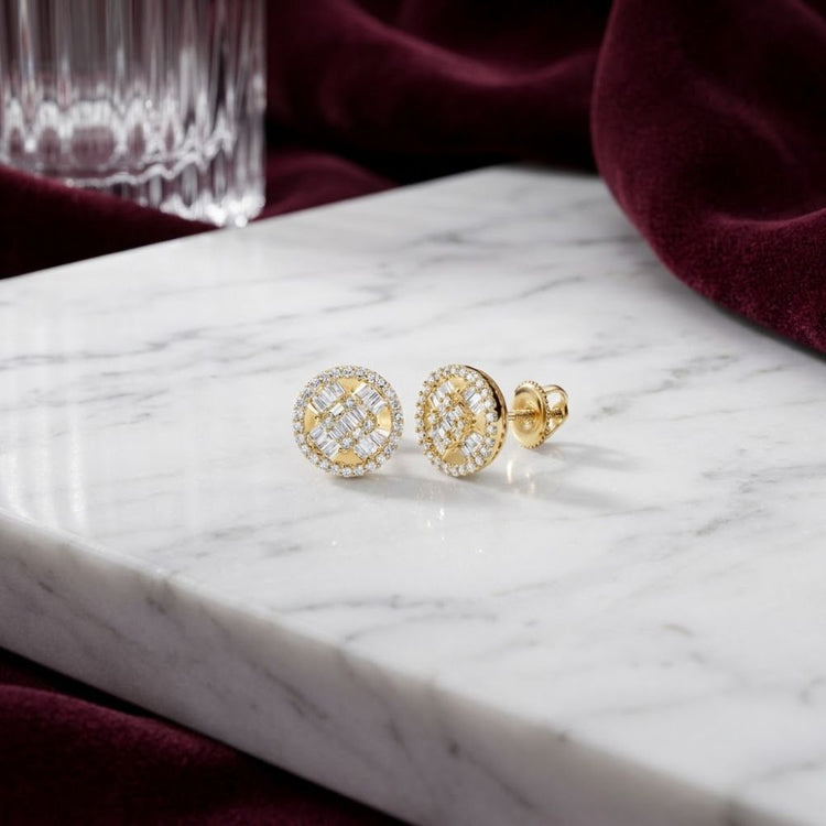A pair of 10K Gold Baguette Diamond Circle Earrings (5/8 CTW) rest elegantly on a white marble surface, with a crystal glass and rich burgundy fabric in the background.