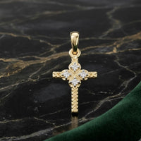 The 1/20CTW Natural Diamond Cross Pendant in 10K gold features intricate detailing with natural diamonds at the center and ends, shown on dark marble with a green velvet accent.