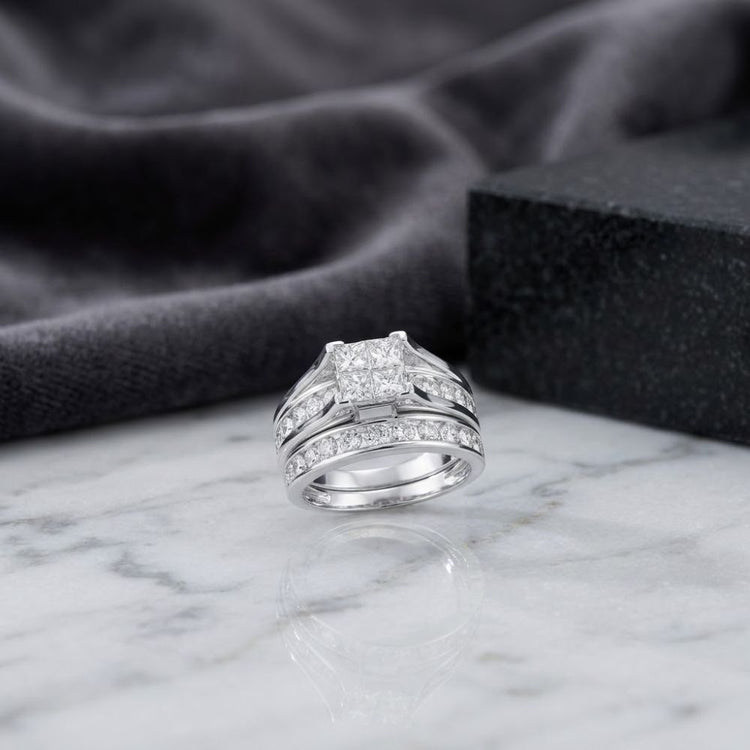 A breathtaking 14K Gold Princess Diamond Bridal Ring Set (2 CTTW) features a square-cut center stone accented by sparkling diamonds, presented on a marble surface with a dark fabric and stone block in the background.