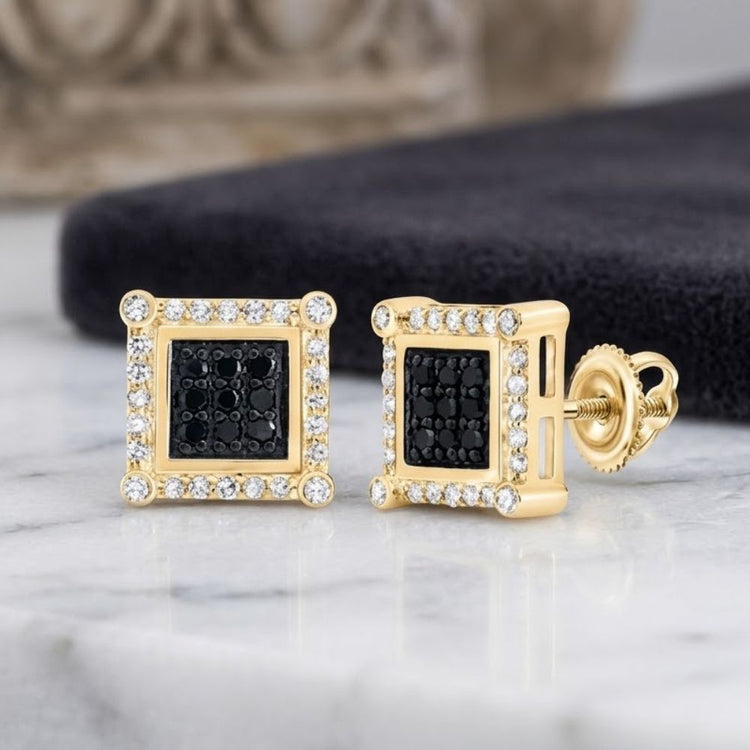 Showcasing timeless sophistication, the 10K Gold Black Diamond Square Earrings 1/4 CTTW feature a central cluster of black diamonds surrounded by a sparkling border of clear stones. Displayed on a marble surface with a dark cloth background, these square earrings offer classic elegance with contemporary appeal.