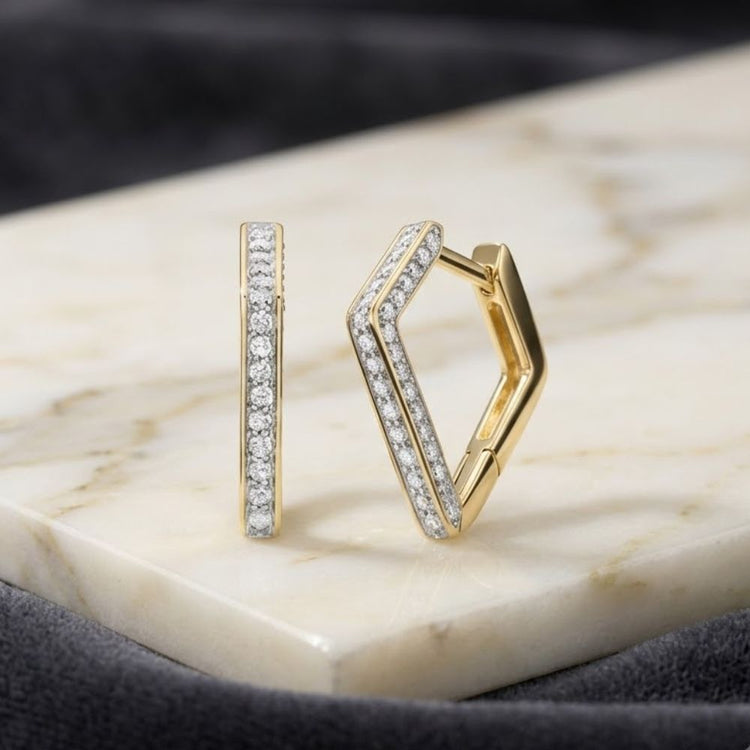 The 1/3 CTW Natural Diamond Huggie Hoop Earrings in 10k gold are displayed on a white marble slab, set against a dark, soft fabric background.
