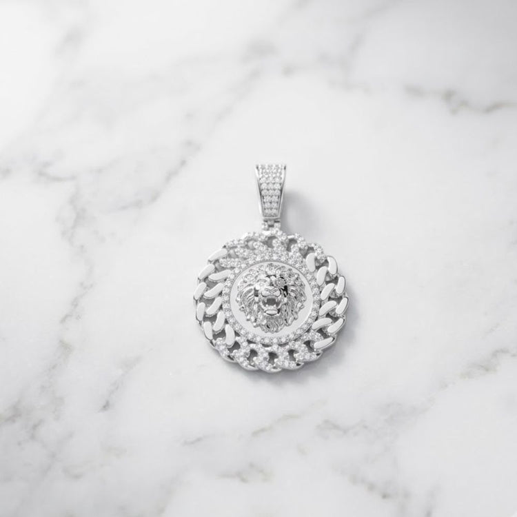 The Diamond Lion Face Cuban Charm 1/2CT Sterling Silver—a bold sterling silver men’s pendant adorned with sparkling diamonds and showcasing a striking lion’s head design—rests elegantly on a white marble surface, embodying the essence of Cuban round men's jewelry.