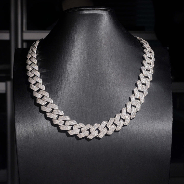 The Moissanite Cuban Links Chain 18mm, crafted from 925 Sterling Silver and encrusted with sparkling stones, is showcased on a black mannequin bust against a dark background.