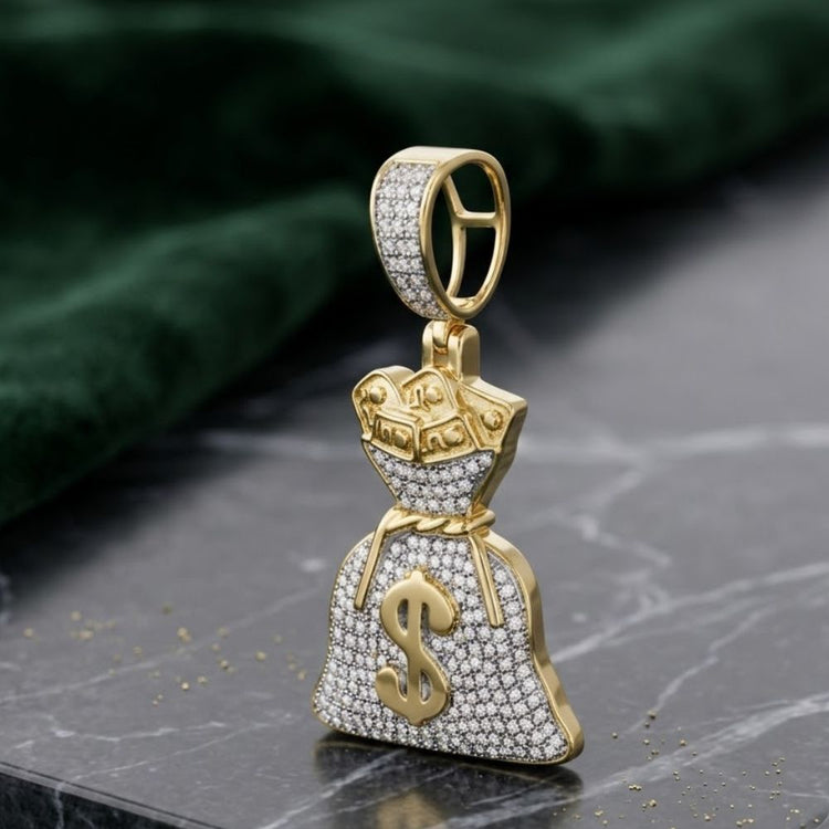 The 10K Gold Diamond Money Bag Pendant 1/2 CTTW, shaped like a dollar sign, rests on dark marble with green fabric in the background, creating a luxurious setting for this standout diamond charm.