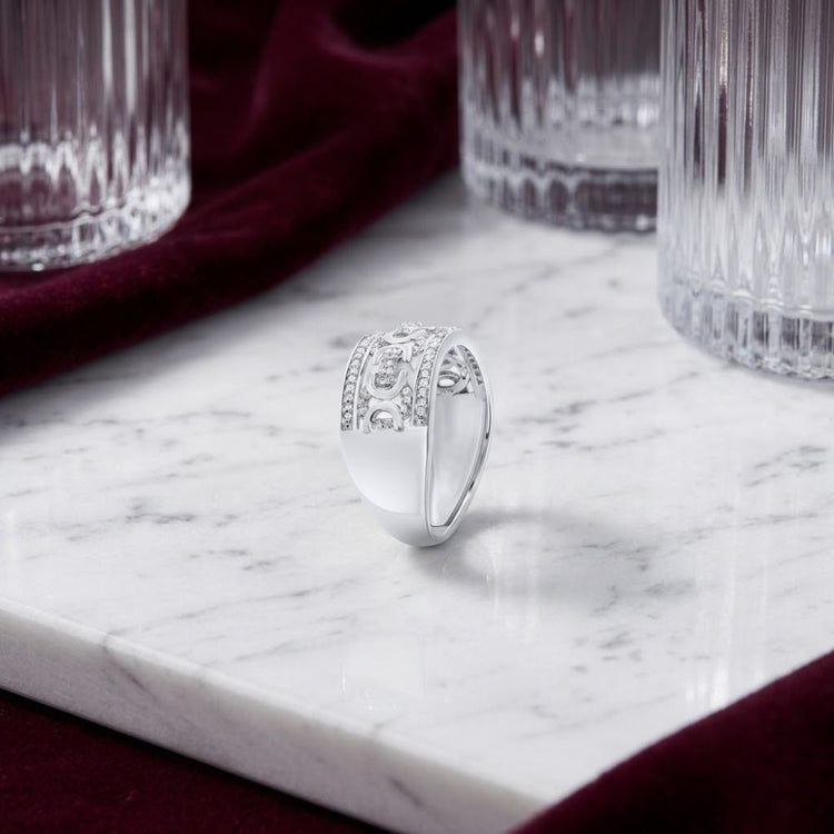 A 1/3 CT Natural Diamond Men’s Ring in Sterling Silver rests on a white marble surface, surrounded by ribbed glass tumblers and a burgundy velvet cloth. This striking design brings timeless elegance to any collection.