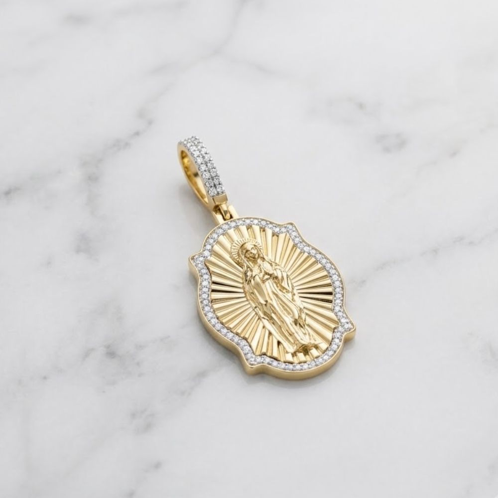The Diamond Virgin Prayer Charm 3/8CT 10K Gold, featuring a raised religious figure surrounded by radiating lines and bordered with diamonds, rests on a white marble surface.
