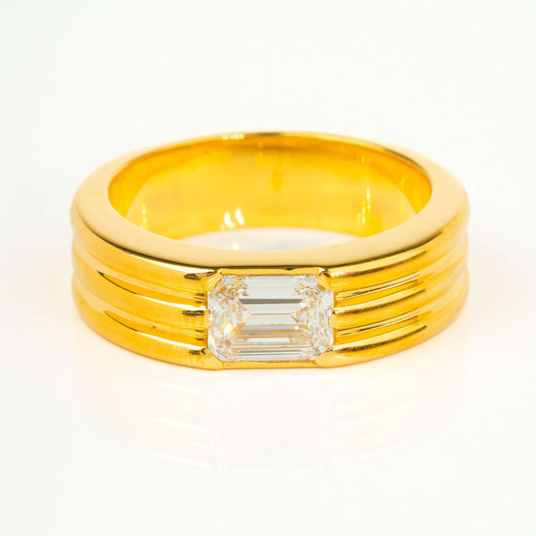 The 2 CT Emerald Diamond Statement Ring features a gold band with three horizontal grooves and a central rectangular emerald-cut diamond, shown on a white background.