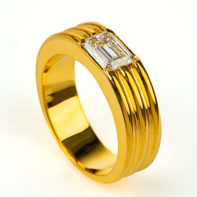 The 2 CT Emerald Diamond Statement Ring features three parallel grooves and a stunning emerald-cut diamond at its center, elegantly showcased on a white background.