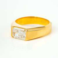 The 2 CT Radiant-Cut Diamond Statement Ring features a large rectangular diamond set flush in a wide 18K yellow gold band, reflecting light beautifully as it rests on a white surface.