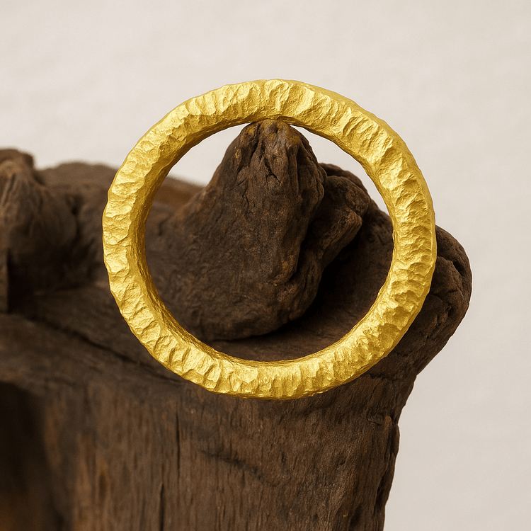 The 24k - 4mm Hammered Donut Ring, featuring a textured finish, is displayed on rugged, weathered wood with a neutral background.