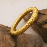 The 24k - 4mm Hammered Donut Ring features a textured, matte finish that enhances its rustic and handcrafted look against natural brown stone surfaces.
