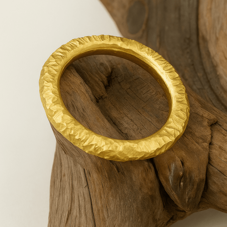 The 24k - 4mm Hammered Donut Ring, featuring a textured finish, is displayed on driftwood against a light background.