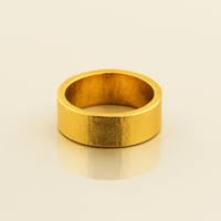The 8mm Flat Band Ring - 24k, featuring a wide, plain matte finish, stands upright on a neutral reflective surface.