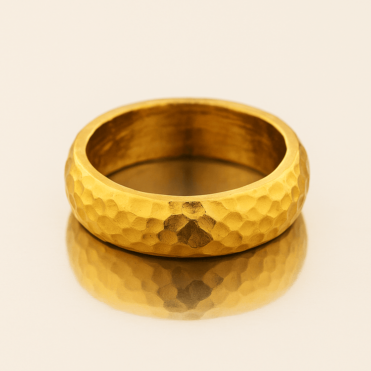 The 8mm Hammered Band Ring - 24k rests on a reflective surface, showcasing its matte finish, rounded edges, and comfort-fit hammered texture.