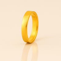 The 4mm Flat Band Ring - 24k stands upright on a light-reflective surface, displaying a subtle textured finish and soft shadows against a beige background.