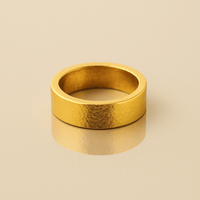 The 6mm Flat Band Ring -24k, featuring a wide, matte finish, rests on a smooth beige surface with a gentle shadow and reflection below.
