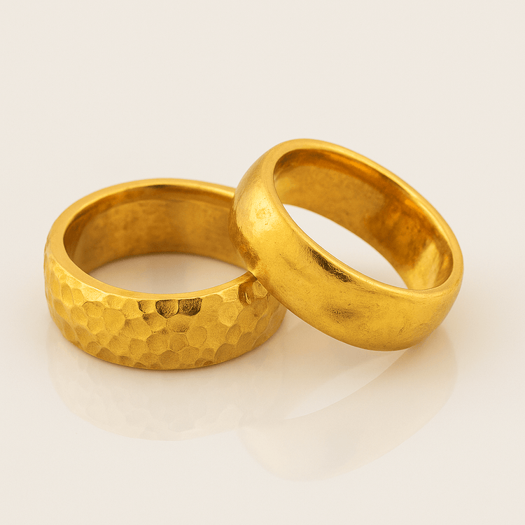 The 8mm Band Ring -24k rests on a light surface, featuring one smooth comfort-fit band and another with a unique hammered texture.