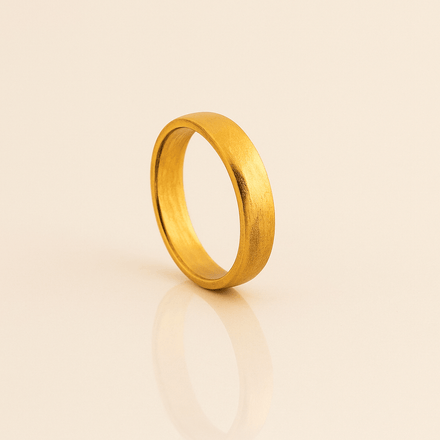 The 6mm Band Ring 24k stands upright on a smooth, reflective beige surface, casting a soft shadow. This comfort-fit ring features a matte finish and a simple, unadorned design.
