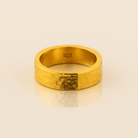 The 6mm, 24k Hammered Flat Band features a comfort-fit design with a unique darker hammered section on one side, displayed on a light beige surface.