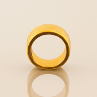 The 10mm, 24k 1oz Hammered Flat Band features a matte finish, smooth edges, and a comfort-fit design for everyday elegance. It stands upright on a neutral, reflective surface, showcasing its wide hammered texture.