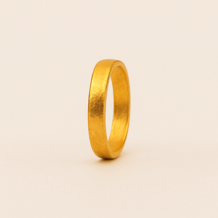 A 4mm, 24k band ring with a smooth, slightly matte finish and no engravings stands upright on a light beige background.