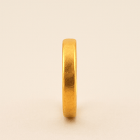 A 4mm, 24k Band Ring stands upright on a neutral background, its smooth and slightly reflective surface showcasing the timeless comfort-fit design.