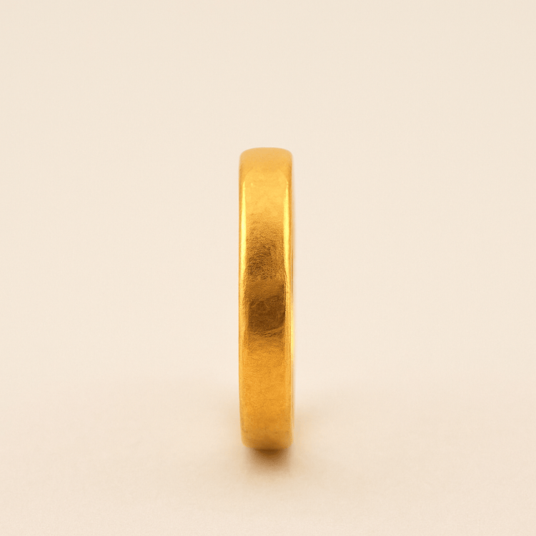 A 4mm, 24k Band Ring stands upright on a neutral background, its smooth and slightly reflective surface showcasing the timeless comfort-fit design.