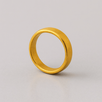 The 4mm, 24k Band Ring features a smooth, plain gold finish and stands upright on a light gray surface against a neutral background.