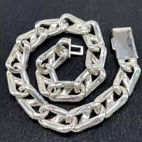 The Ice Out Silver Moissanite Cuban Link Chain - 20mm, featuring thick, shiny sterling silver rectangular links and a bold clasp, rests on a dark surface.
