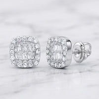 The 1/4CTW Natural Diamond Cushion Baguette Earrings in 10K gold feature a square-shaped design accented by a halo of sparkling smaller diamonds. These earrings are showcased on a light marble surface and are crafted with shiny 10k gold settings and secure screw-back posts.