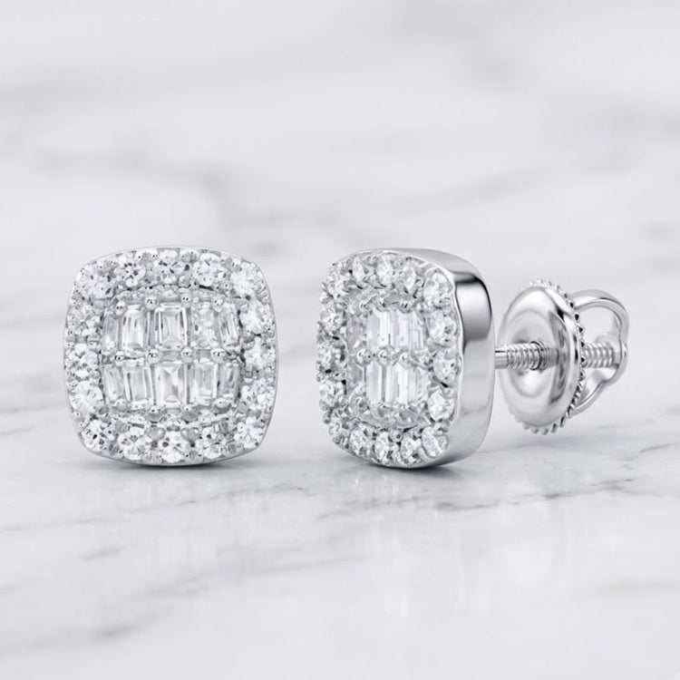 The 1/4CTW Natural Diamond Cushion Baguette Earrings in 10K gold feature a square-shaped design accented by a halo of sparkling smaller diamonds. These earrings are showcased on a light marble surface and are crafted with shiny 10k gold settings and secure screw-back posts.