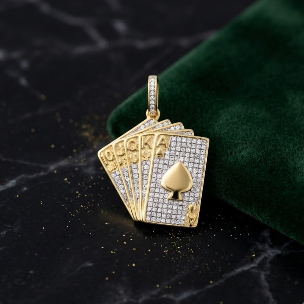 The 10K Gold Diamond Royal Flush Pendant 5/8 CTTW, shaped like five spade playing cards and set with diamonds, sits on a black marble surface beside a green velvet pouch.