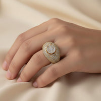 A hand rests on soft beige fabric, adorned with the Domed Pavé Diamond Ring – 5.84 CT Gold Design, a bold men's ring encrusted with multiple rows of sparkling white diamonds.