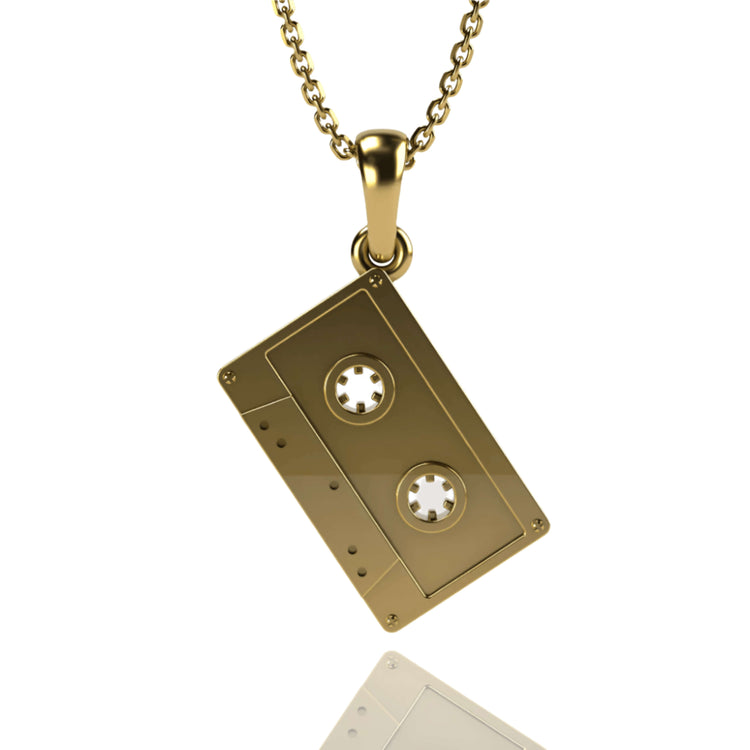 The 14k Gold Cassette Tape Pendant, ideal for music lovers, showcases intricate reels and vintage-inspired edges. Displayed on a plain white background with a subtle reflection below.