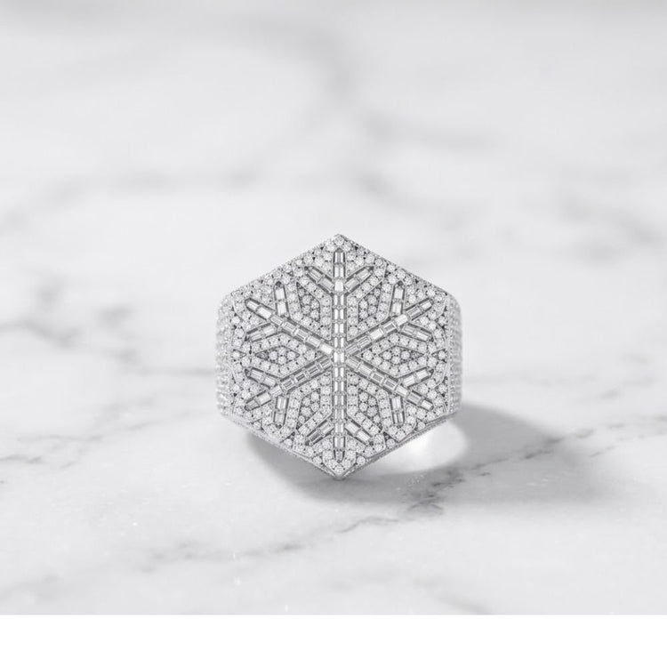 The 925 Silver Moissanite Snowflake Ring features a hexagonal design with an intricate snowflake pattern, set with sparkling moissanite stones, displayed on a white marble surface.